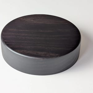 Può includere: Un coperchio rotondo in legno nero con una superficie liscia e lucida.