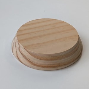 May include: A round wooden display stand with a natural wood finish. The stand has a slightly raised edge and a smooth surface.