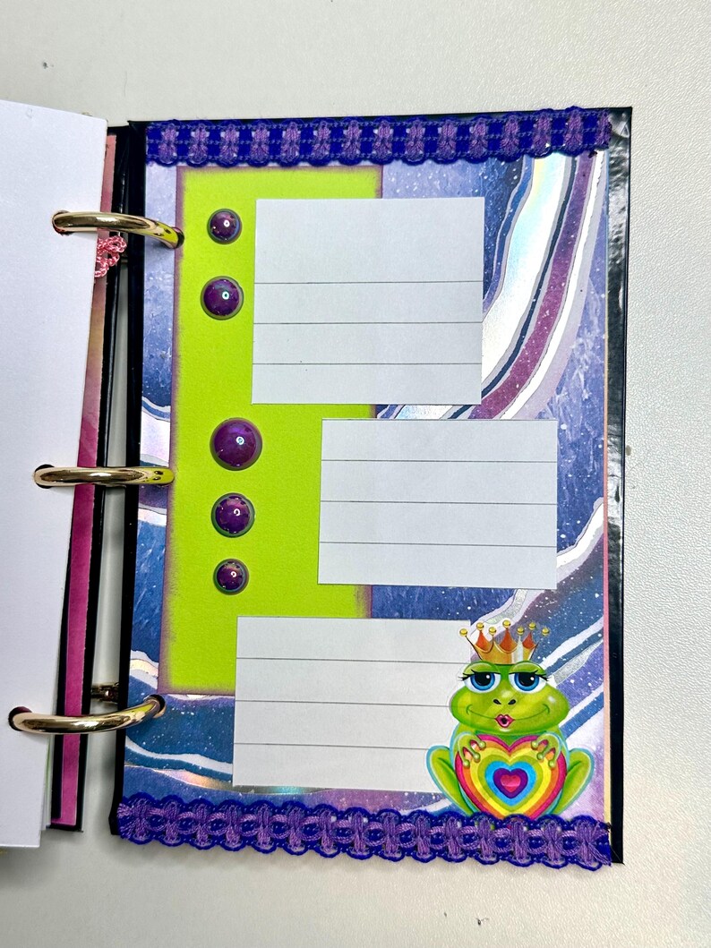 Puede incluir: Una p&aacute;gina de planificador colorida con una secci&oacute;n verde lima con tres cuadros rayados para notas. Acentos de gemas moradas y un borde decorativo enmarcan la p&aacute;gina. Una rana de dibujos animados con una corona y un coraz&oacute;n est&aacute; en la esquina.