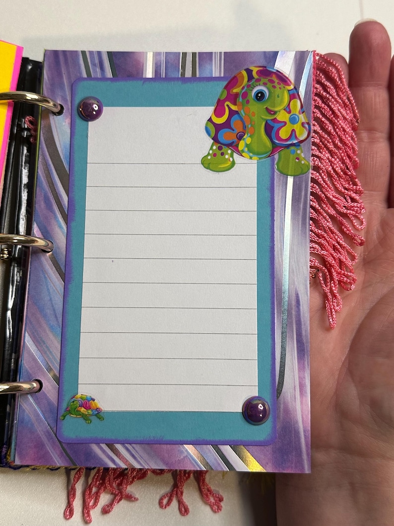 Puede incluir: Una p&aacute;gina de cuaderno colorida con un borde turquesa y papel rayado. Una pegatina de tortuga de dibujos animados con un dise&ntilde;o floral est&aacute; en la parte superior, y una pegatina de tortuga m&aacute;s peque&ntilde;a en la parte inferior. La p&aacute;gina est&aacute; decorada con detalles morados y flecos rosas.