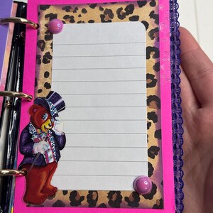Puede incluir: Una p&aacute;gina de diario hecha a mano con un borde rosa brillante, fondo de estampado de leopardo y papel rayado. Un oso de dibujos animados con sombrero de copa y traje est&aacute; a la izquierda. Dos chinchetas rosas aseguran el papel. Ribete de encaje morado a la derecha.