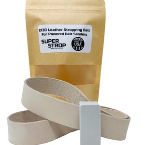 Puede incluir: Una correa de afilado de cuero de 1x30 pulgadas para lijadoras de banda eléctricas. La correa es beige y viene en una bolsa de papel marrón con el texto "1x30 Leather Stropping Belt for Powered Belt Sanders" y "SUPER STROP" con una bandera estadounidense roja, blanca y azul con el texto "MADE IN USA".