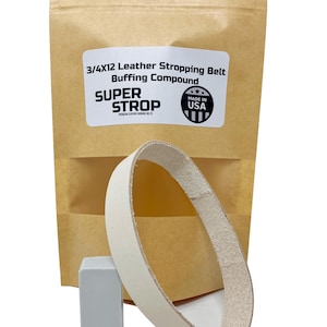 Puede incluir: Un cinturón de cuero para afilar con un compuesto de pulido, un bloque rectangular gris y un paquete de papel marrón. El paquete tiene el texto "3/4x12 Leather Stropping Belt Buffing Compound SUPER STROP MADE IN USA". El cinturón mide unos 30 cm de largo.