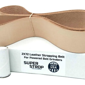 Puede incluir: Una correa de afilado de cuero color beige para amoladoras de banda motorizadas, enrollada y asegurada con una banda elástica. La correa se muestra con una caja blanca que dice "2X72 Leather Stropping Belt" y "Super Strop". También hay un pequeño tubo de papel enrollado.