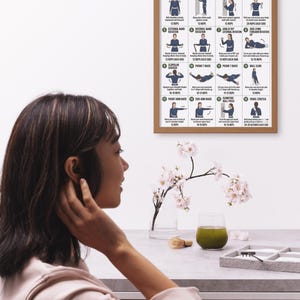 May include: A framed poster titled "Rotator Cuff Exercises" with illustrations of shoulder mobility and strength exercises. A woman is seen in the foreground, with a glass of green liquid and flowers on a table.