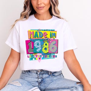 May include: White t-shirt with a colorful graphic that reads "MADE IN 1986 LIMITED EDITION." The design features the numbers 1986 in a retro style with vibrant colors and patterns. The shirt is a casual wear item.