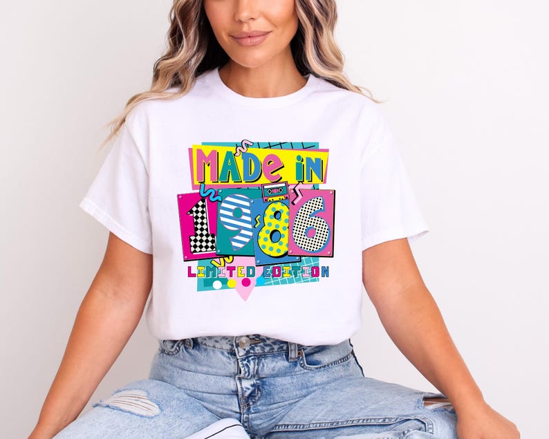 May include: White t-shirt with a colorful graphic that reads "MADE IN 1986 LIMITED EDITION." The design features the numbers 1986 in a retro style with vibrant colors and patterns. The shirt is a casual wear item.