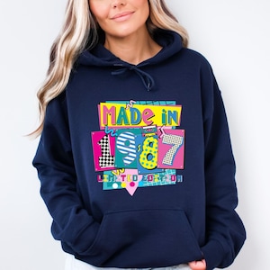 Może przedstawiać: Granatowa bluza z kapturem z kolorową grafiką z napisem "MADE IN 1987 LIMITED EDITION". Grafika zawiera cyfry 1, 9, 8 i 7 w r&oacute;żnych kolorach i wzorach, w tym czarno-białą szachownicę.