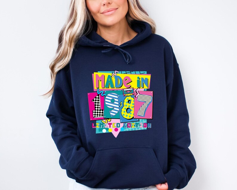 Może przedstawiać: Granatowa bluza z kapturem z kolorową grafiką z napisem "MADE IN 1987 LIMITED EDITION". Grafika zawiera cyfry 1, 9, 8 i 7 w r&oacute;żnych kolorach i wzorach, w tym czarno-białą szachownicę.