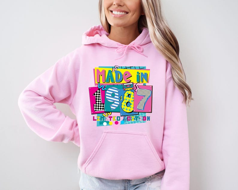 Może przedstawiać: Jasnor&oacute;żowa bluza z kapturem z kolorową grafiką z przodu z napisem "MADE IN 1987 LIMITED EDITION". Grafika ma styl retro, z cyfrą 8 w kolorze ż&oacute;łtym i turkusowym obrysem.