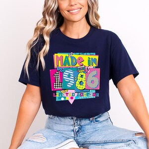 May include: Navy blue t-shirt with a colorful graphic that reads "MADE IN 1986 LIMITED EDITION." The graphic features the numbers 19 and 86 in a retro style with vibrant colors and patterns. The shirt is being worn.