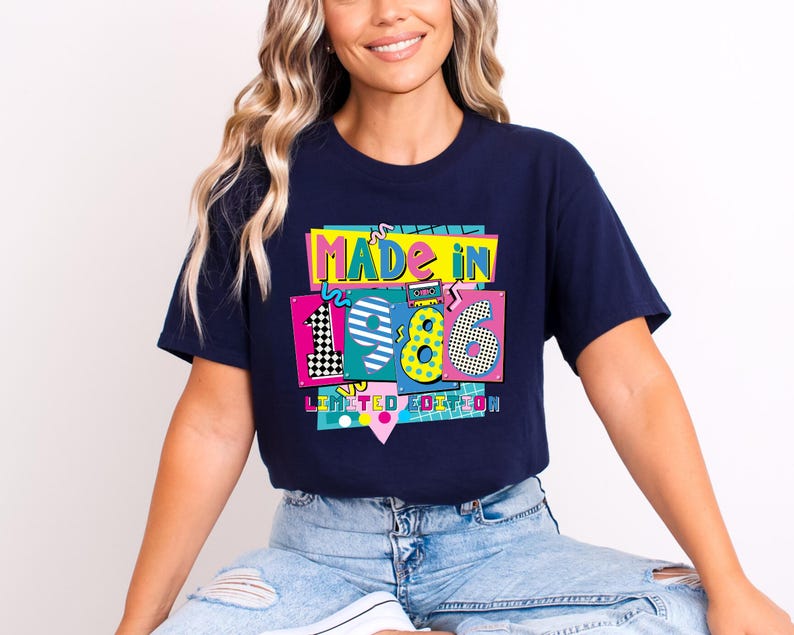 May include: Navy blue t-shirt with a colorful graphic that reads "MADE IN 1986 LIMITED EDITION." The graphic features the numbers 19 and 86 in a retro style with vibrant colors and patterns. The shirt is being worn.