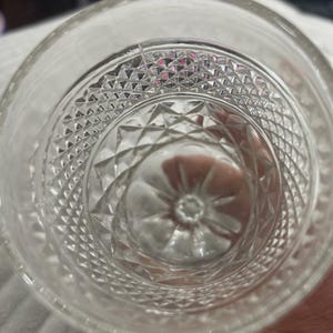 May include: Clear glass tumbler with a diamond pattern on the bottom and sides. The glass has a thick base and a smooth rim. The design is visible from the inside of the glass.