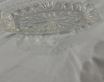 May include: A clear, rectangular glass dish with a starburst design in the center. The edges of the dish are scalloped. The dish is likely used for serving or display.