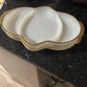 Puede incluir: Dos platos de servir de vidrio de leche blanco con ribete dorado. Los platos son de forma ovalada y tienen tres secciones.