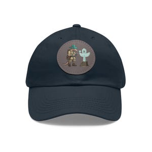 Peut inclure: Une casquette de baseball bleu marine avec un patch marron représentant un fourmilier de dessin animé tenant une loupe et regardant un ankh en pierre.