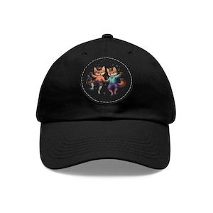 May include: Black baseball cap featuring a circular patch with two cartoon foxes. The foxes are depicted in colorful outfits, with one in orange and green, and the other in purple and blue. The patch is outlined with a white dotted line.