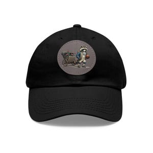 May include: Black baseball cap with a round patch featuring a cartoon raccoon pushing a cart full of flowers. The raccoon is wearing a blue jacket and white pants.