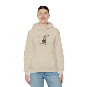 May include: A beige hoodie with a kangaroo graphic. The kangaroo is wearing a hat and holding a teacup and a flag. The text around the kangaroo reads "Kangaroo Dreams Keep Moving Little One".