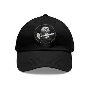 May include: A black baseball cap with a white and gray patch featuring a cartoon beaver holding a baguette. The patch has a stitched border.