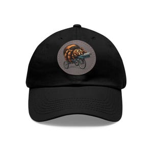 May include: Black baseball cap featuring a circular patch with a cartoon spider riding a bicycle with a delivery box. The spider is brown and orange, and the bicycle is blue. The patch is on a black cap.