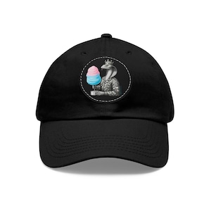 Peut inclure: Casquette de baseball noire avec un écusson rond représentant un cobra couronné en uniforme militaire, tenant une barbe à papa. La barbe à papa est rose et bleue. La casquette a une visière incurvée et un bouton sur le dessus.