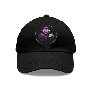 May include: A black baseball cap with a round, white patch featuring a cartoon vulture wearing a cape and holding a tablet. The vulture has purple feathers and a red beak.