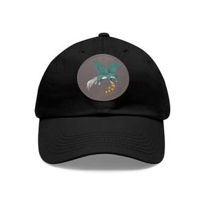 May include: Black baseball cap with a round patch featuring a teal winged creature with a white tail and gold coins. The cap has a curved brim and a fabric strap closure.