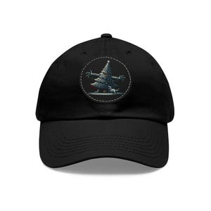 May include: Black baseball cap with a curved brim. The cap features a circular patch with a cartoon Christmas tree design, complete with arms and a small dog. The tree is dark green with white accents, set against a white background.
