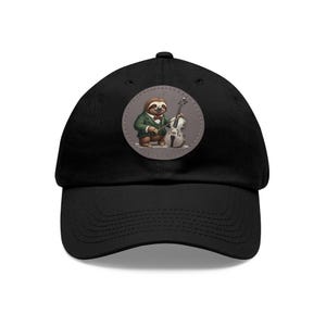 May include: Black baseball cap featuring a circular patch with a cartoon sloth playing a cello. The sloth is dressed in a green blazer and bow tie. The cello is white and gray. The cap has a curved brim and a fabric strap closure.