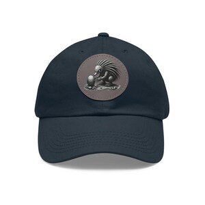 May include: A navy blue baseball cap with a round patch featuring a gray and white echidna holding an egg. The patch has a brown stitched border.