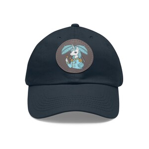 May include: Navy blue baseball cap with a circular patch featuring a cartoon unicorn in a blue military-style jacket. The unicorn holds a small object and is surrounded by blue feather-like shapes. The cap has a curved brim.