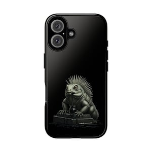 Puede incluir: Funda de teléfono negra con una ilustración detallada de una iguana verde con cresta espinosa. La iguana está colocada sobre una superficie oscura y texturizada. La funda tiene un acabado brillante y una configuración de doble cámara.