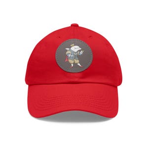 May include: A bright red baseball cap featuring a circular patch with a cartoon dolphin dressed in regal attire, including a crown and cape. The dolphin is holding a small object. The cap is made of a soft material.
