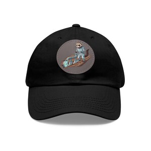 May include: Black baseball cap with a circular patch featuring a cartoon ferret in a spacesuit operating a plow. The patch has a brown background and the ferret is wearing a blue and white spacesuit. The cap has a curved brim.
