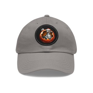 May include: A gray baseball cap featuring a circular patch with a festive design. The patch depicts a cartoon ostrich wearing a Santa hat and a formal collar, inside a Christmas ornament. The ornament has a red and orange gradient.