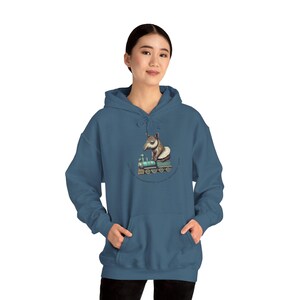 May include: A dark blue hooded sweatshirt featuring a graphic of a tapir riding a train. The graphic is in a vintage style and includes the text "Sometimes you just have to take the train to adventure".