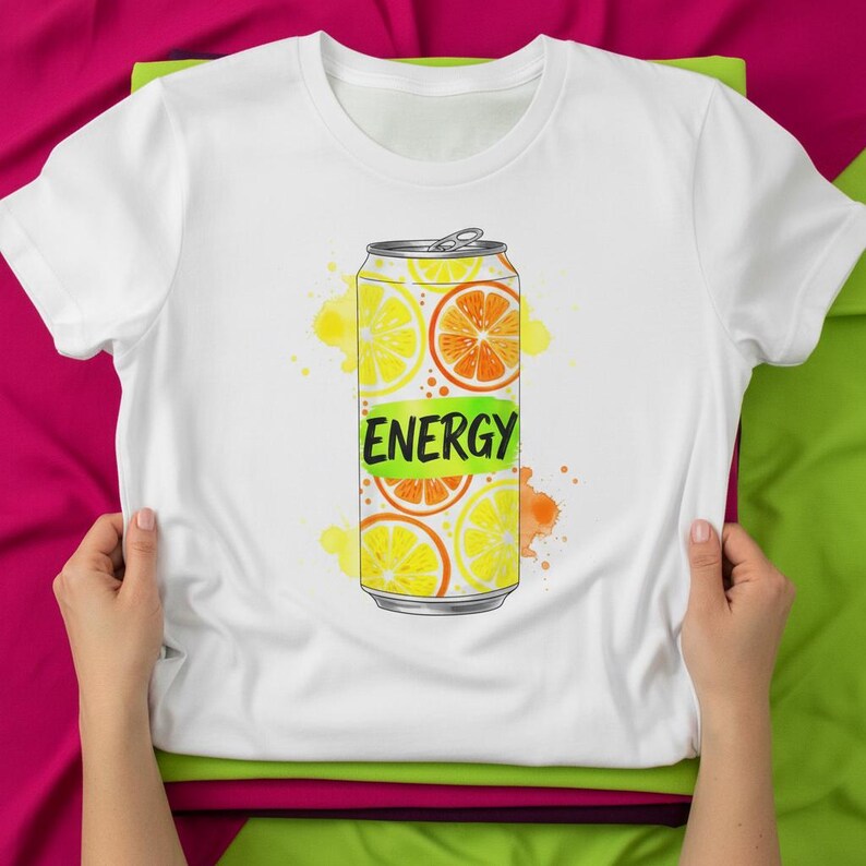 K&ouml;nnte beinhalten: Wei&szlig;es T-Shirt mit einem farbenfrohen Aufdruck einer Limonaden-Dose mit Zitronen- und Orangenscheiben. Das Design der Dose enth&auml;lt das Wort "ENERGY" in Gr&uuml;n. Das Design umfasst gelbe und orangefarbene Aquarellspritzer.