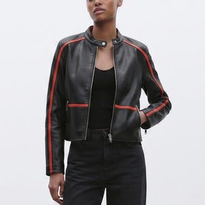 Puede incluir: Una chaqueta de piel sintética negra con cuello mao, cremallera frontal completa y rayas de carreras de color naranja vibrante que recorren el largo de cada manga y la cintura. La chaqueta incluye dos bolsillos laterales con cremallera.