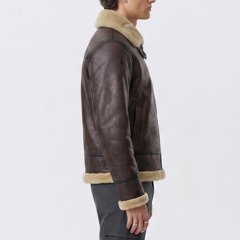 May include: A dark brown jacket with a beige shearling collar and cuffs. The jacket features a smooth exterior finish, a front zipper closure, and a straight hemline that sits at the waist. The design includes visible seam detailing along the sleeves.