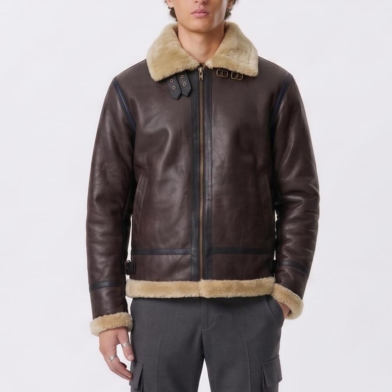 May include: A dark brown leather jacket featuring a tan shearling collar and lining. The jacket includes a full-length front zipper, two adjustable buckle straps at the neck, and matching buckle straps at the waist for a secure fit.