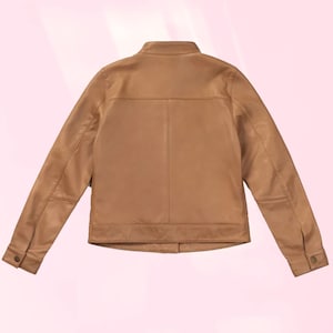 Puede incluir: Chaqueta de cuero color marr&oacute;n claro con un dise&ntilde;o cl&aacute;sico. La chaqueta presenta un cuello alzado, pu&ntilde;os abotonados y un corte entallado. La parte trasera de la chaqueta es visible, mostrando las costuras y los paneles. La chaqueta es de color neutro.