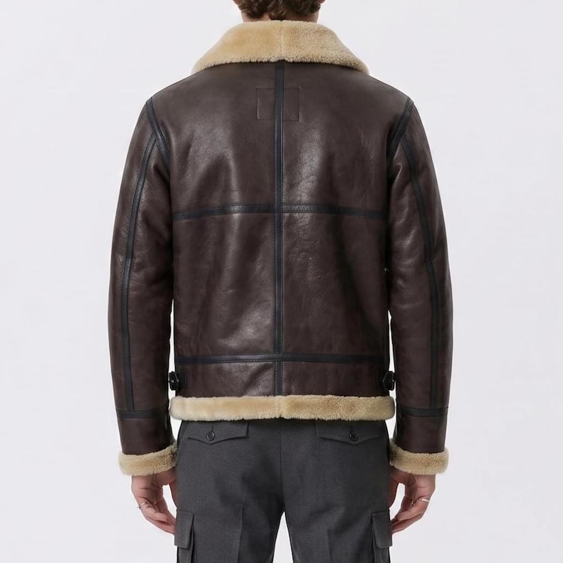 May include: A dark brown leather jacket featuring a tan shearling collar and trim at the cuffs and hem. The jacket has visible dark seam detailing, a structured back panel, and adjustable side tabs at the waist, worn over dark gray trousers.