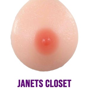 May include: A close-up of a single, flesh-toned silicone breast form with a pink nipple. The form is smooth and appears to be made of a soft, flexible material.
