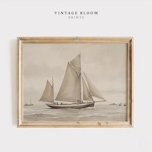 May include: A framed sepia-toned print of a sailboat on the water. The print is in a gold-colored frame and features the text "VINTAGE BLOOM PRINTS" at the top. The sailboat has two masts and sails, and is sailing on a calm sea.