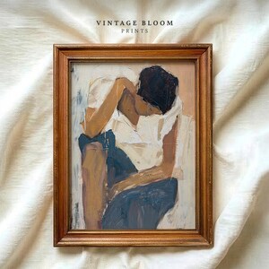 Puede incluir: Una impresión artística enmarcada con un marco de madera dorada. La obra de arte representa a una persona con camisa blanca y pantalón azul, con la cabeza apoyada en el brazo. El texto "VINTAGE BLOOM PRINTS" está en la parte superior.