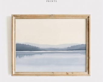 May include: A framed landscape print featuring a serene lake scene with mountains in the background. The artwork is rendered in soft blue and beige tones, with the text "VINTAGE BLOOM PRINTS" at the top. The frame is a light wood color.