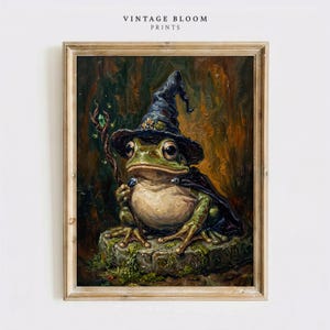 Może przedstawiać: Oprawiony wydruk obrazu olejnego z napisem VINTAGE BLOOM PRINTS przedstawia zieloną żabę w ciemnoniebieskim, spiczastym kapeluszu czarodzieja i pasującej pelerynie. Żaba siedzi na omszałym kamieniu, trzymając w dłoni skręcony drewniany kostur.