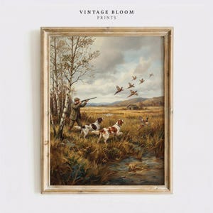 May include: Framed vintage print depicting a hunting scene. A hunter aims a rifle at flying birds, with dogs running through tall grass. The artwork features a muted color palette of greens, browns, and blues, with the text "VINTAGE BLOOM PRINTS" at the top.