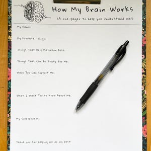 May include: A clipboard with a floral border holds a white sheet of paper with the title "How My Brain Works." The paper includes prompts to fill out, such as "My Favorite Things" and "My Superpowers." A black pen rests on the paper.